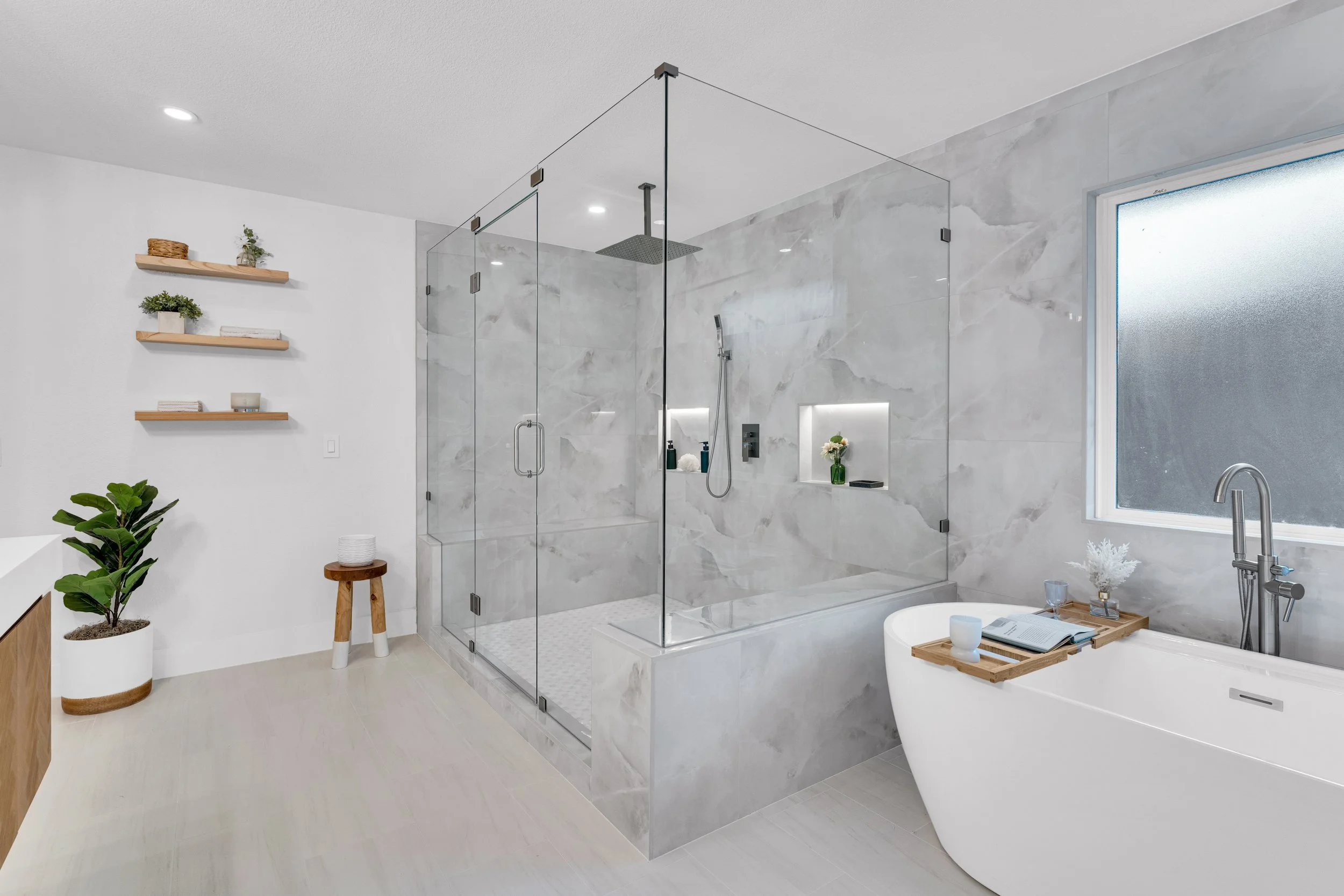 Modern bathroom with a glass-enclosed shower, built-in niche, and a freestanding bathtub, decorated with plants and minimal accessories.