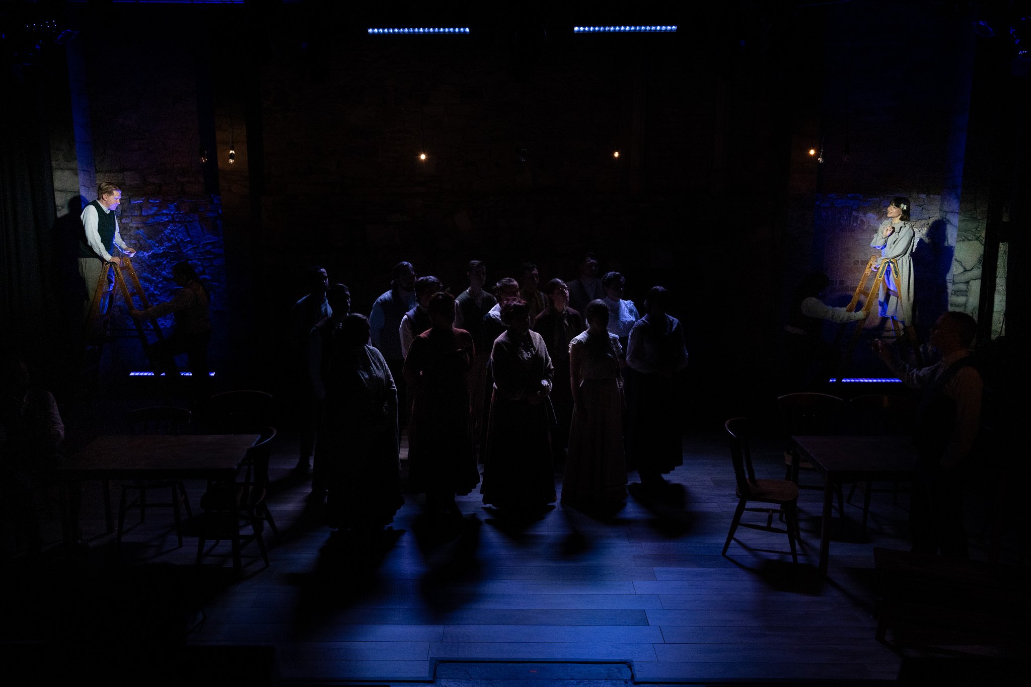 A puppet show with two puppeteers operating puppets above a seated audience in a dark theater with blue lighting.