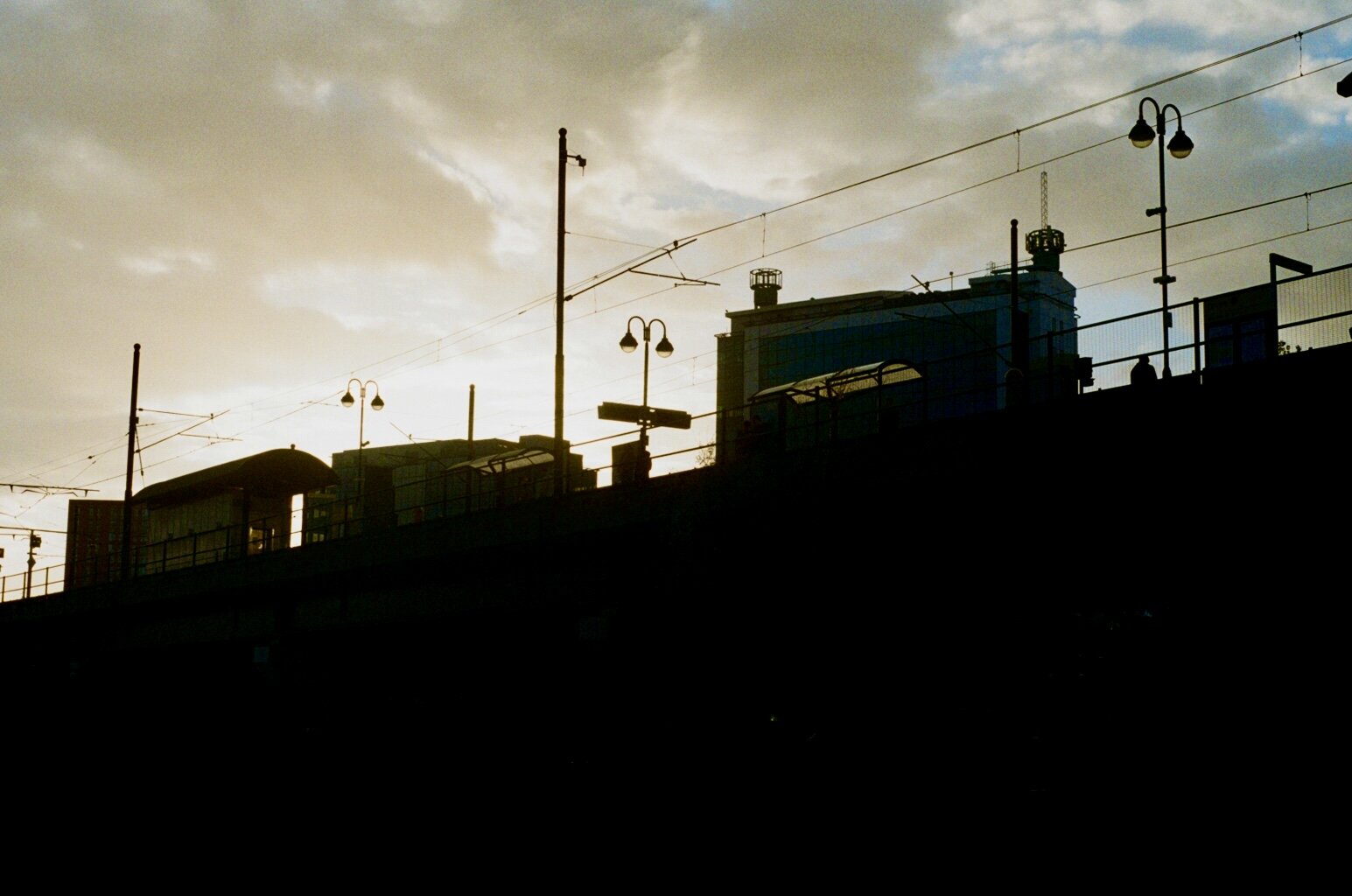 Silhouette of city buildings and streetlights against a cloudy evening sky.
