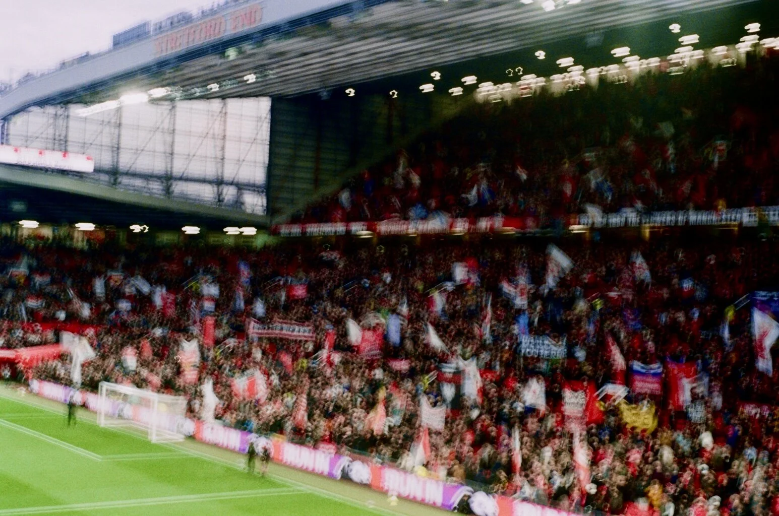 Crowd of soccer fans in stadium stands waving flags and cheering during a game.