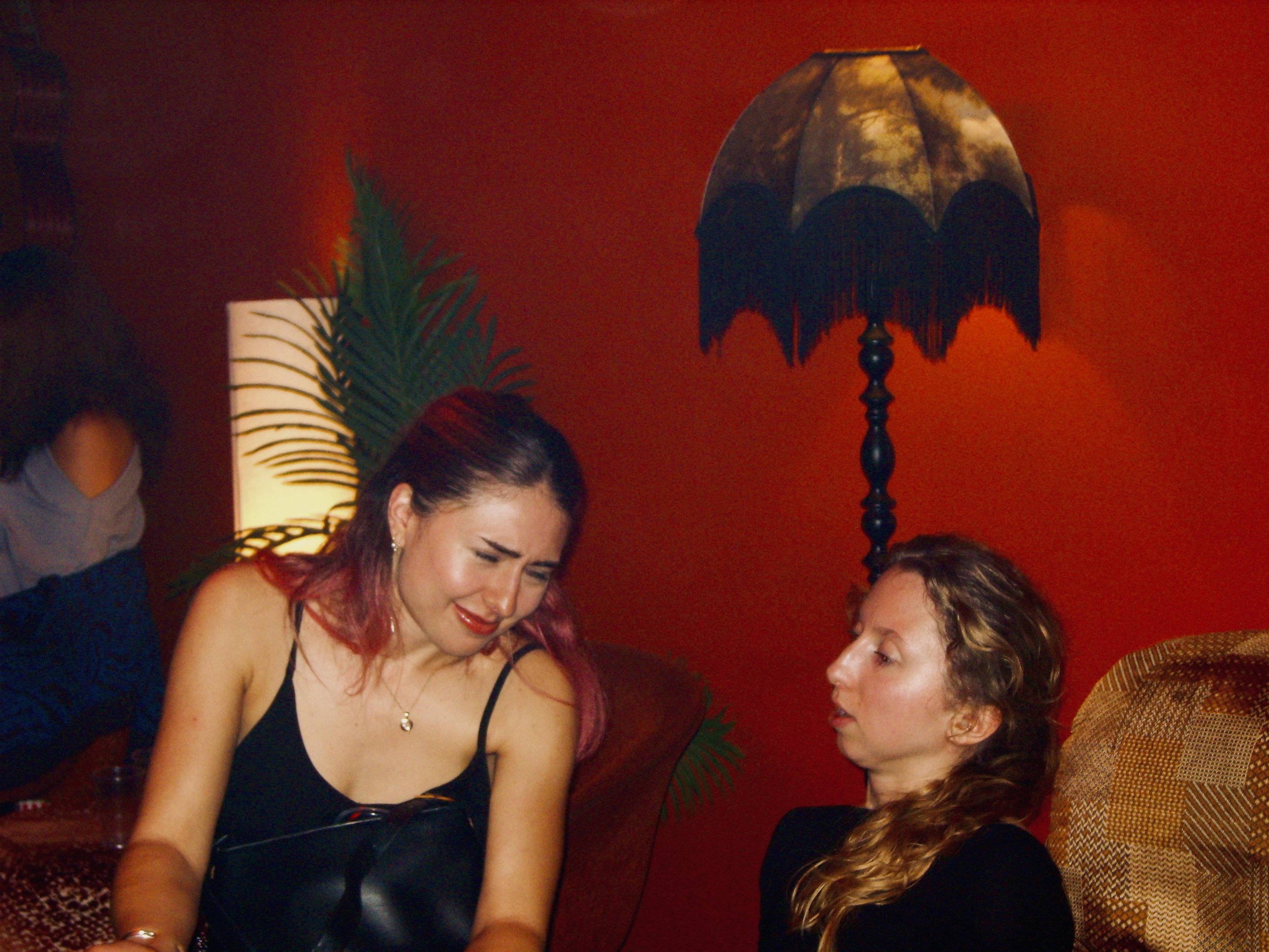 Two women having an emotional moment at a social gathering. One woman with red hair and the other with curly hair are engaged in a close, heartfelt interaction.