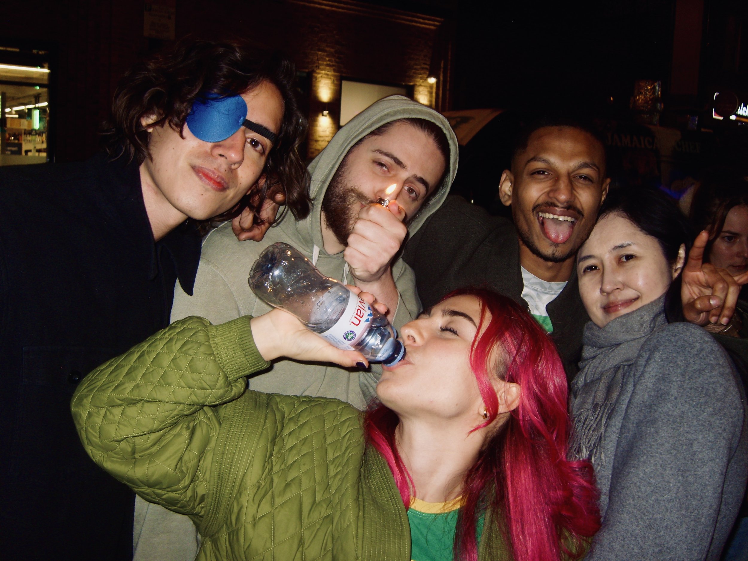Group of people celebrating at an indoor event, with one person drinking from a water bottle and others smiling