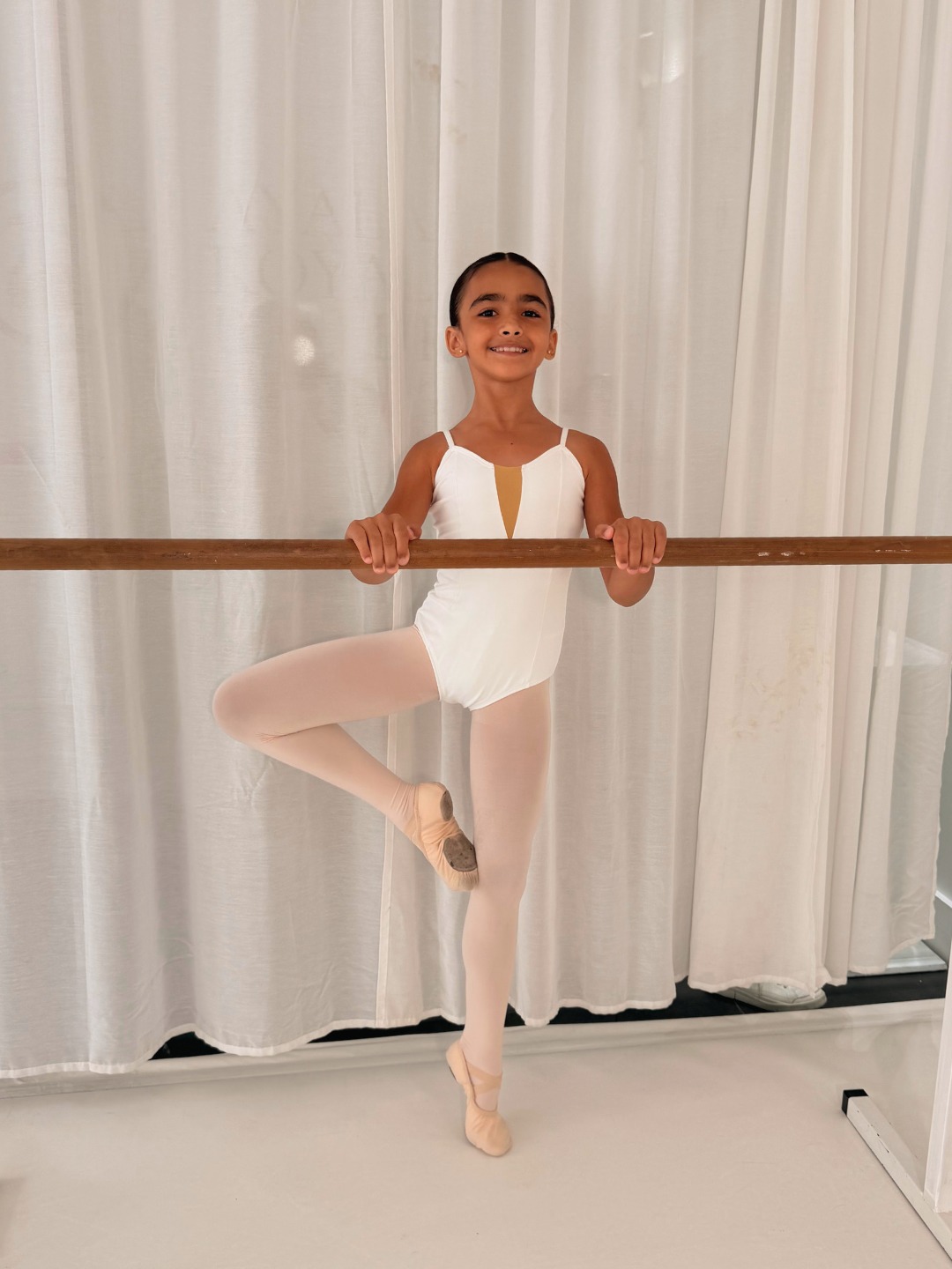 Young girl in ballet attire practicing at a ballet barre in a dance studio
