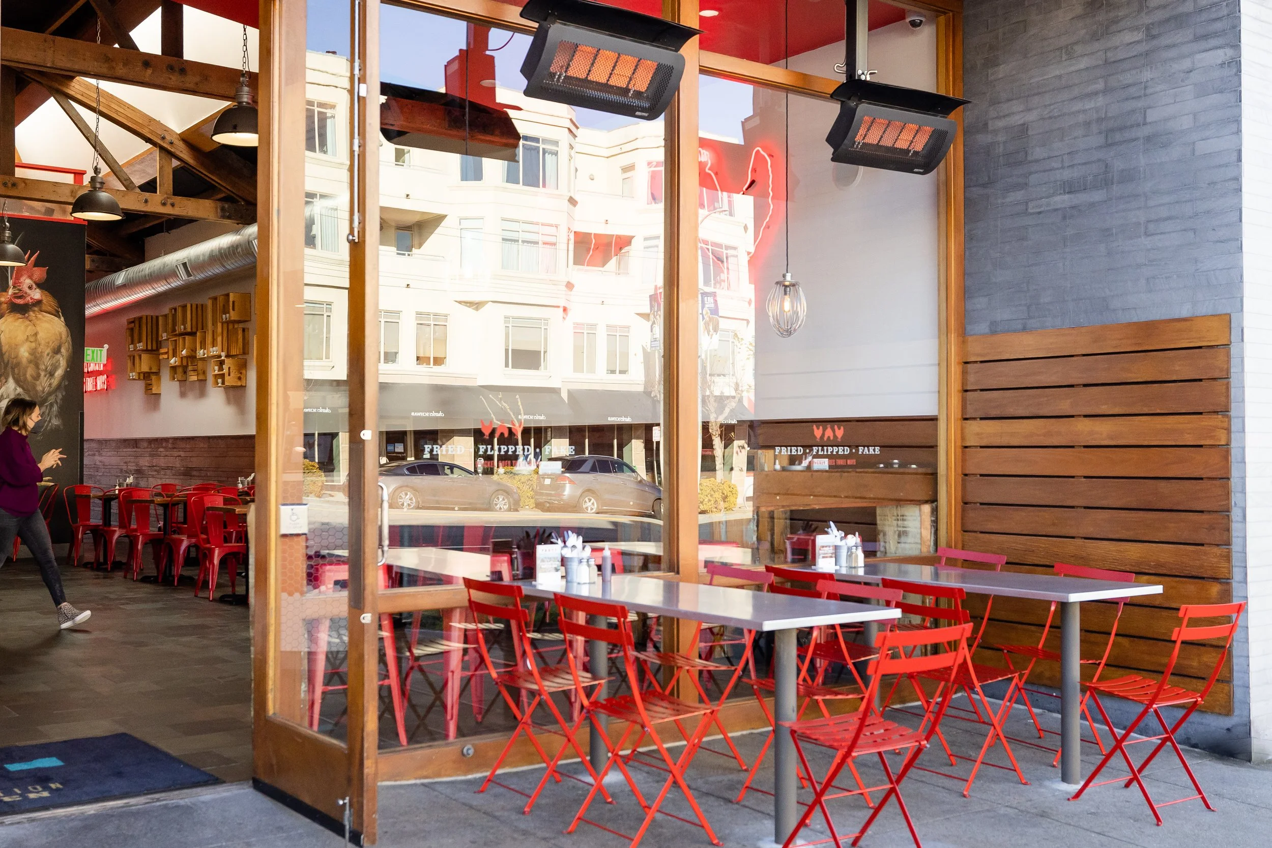 The patio at Proposition Chicken with chairs and tables near large windows. There are wood and metal accents and hanging lights.