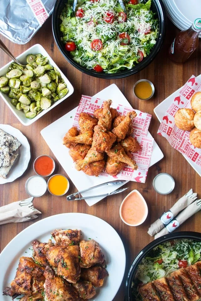 Fried chicken wings with multiple side salads, dipping sauces, and condiments on a wooden table.