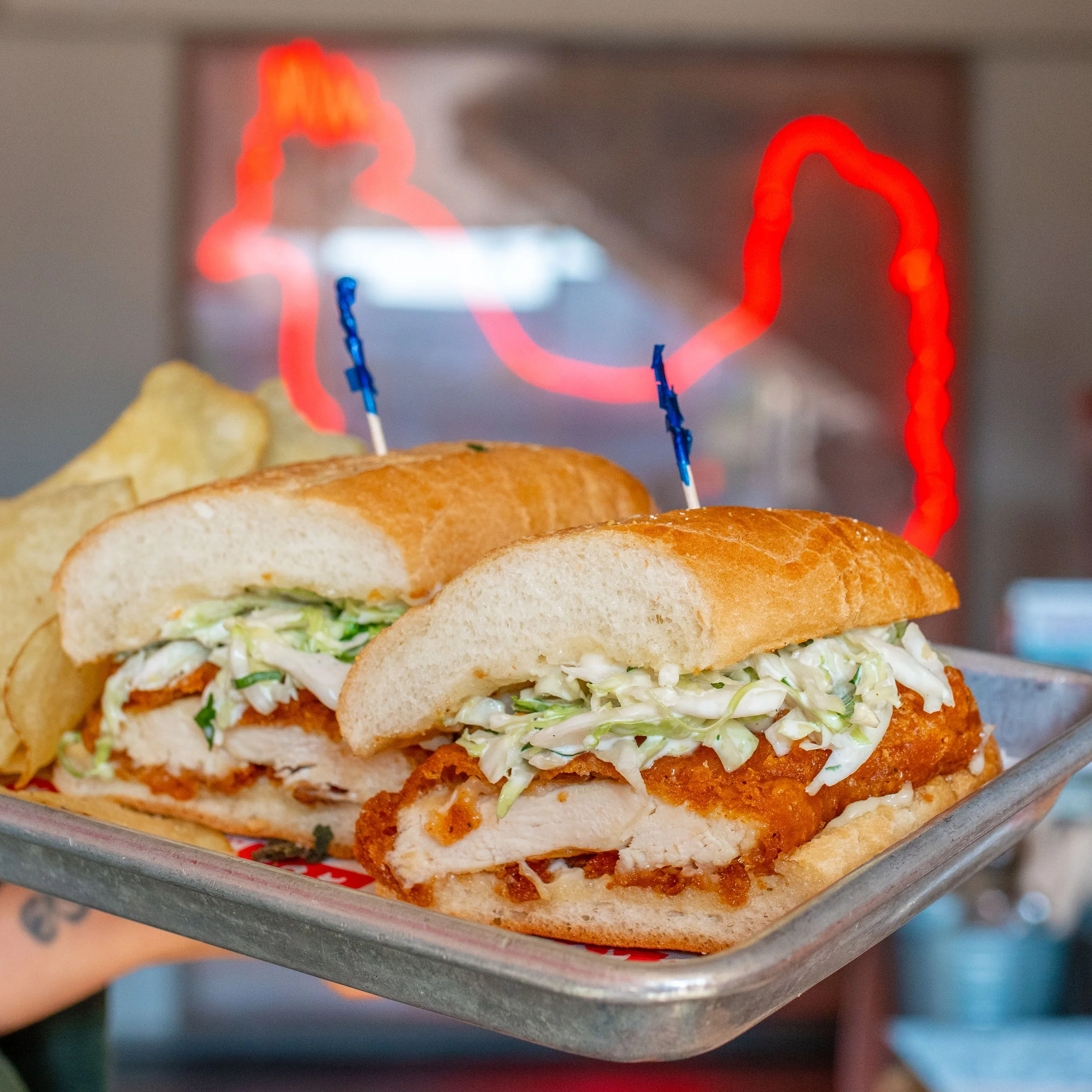 Fried chicken sandwich with shredded lettuce and sauce, with neon lights reflecting on the background.