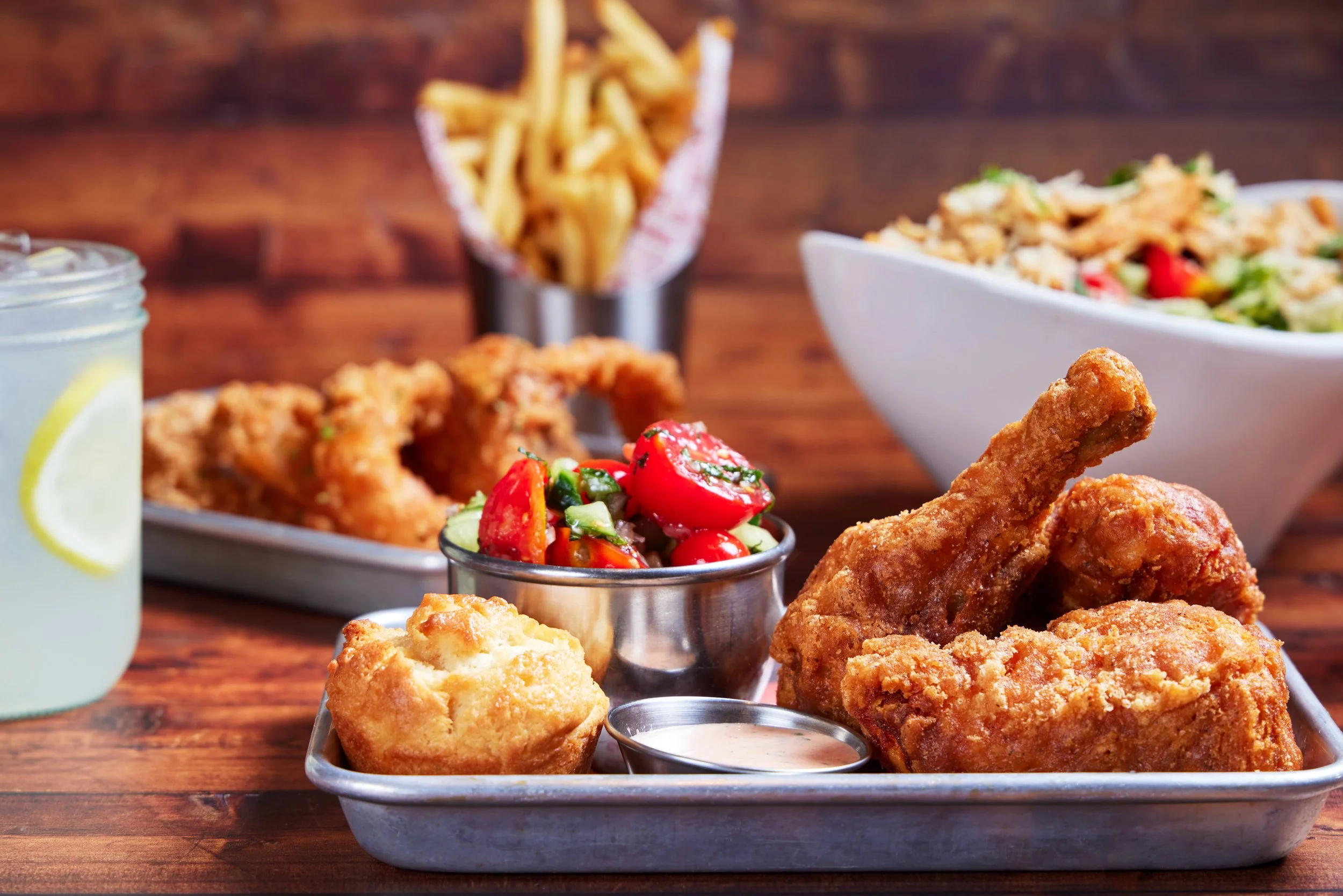 A tray of fried chicken pieces, two biscuits, dipping sauce, and two bowls of salad.