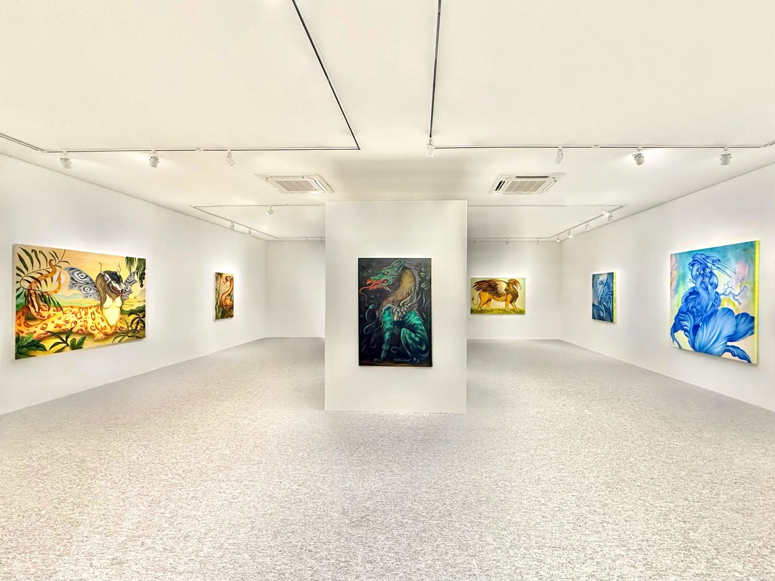 Photo of an art gallery with colorful paintings on white walls and a grey carpeted floor.