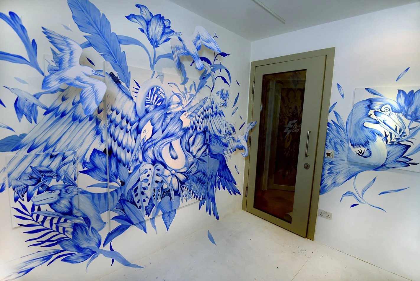 Blue and white mural of various birds and plants on interior walls near a door with glass window.