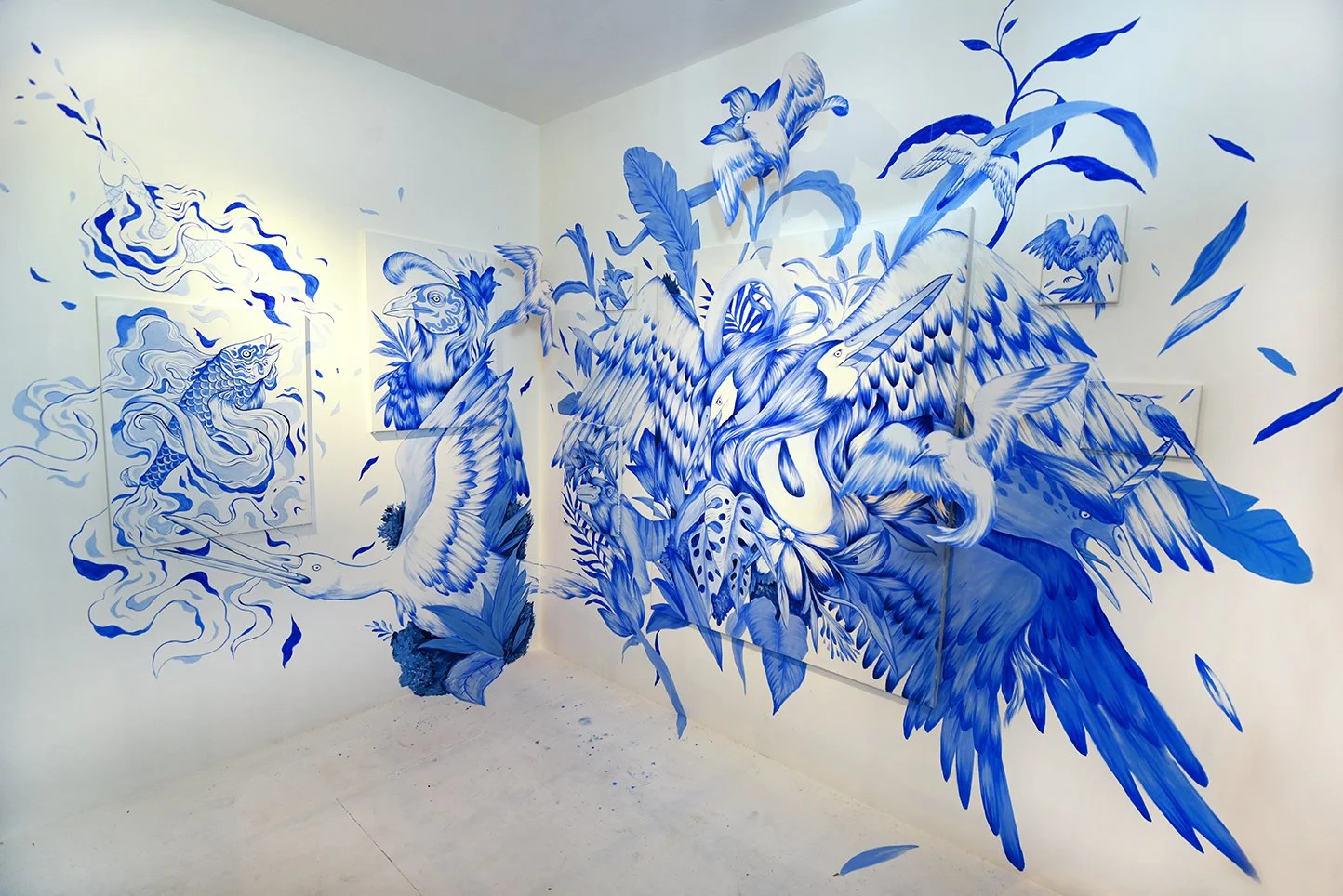 Blue and white mural depicting various birds, fish, and plants, with swirling clouds and abstract designs on a white wall.