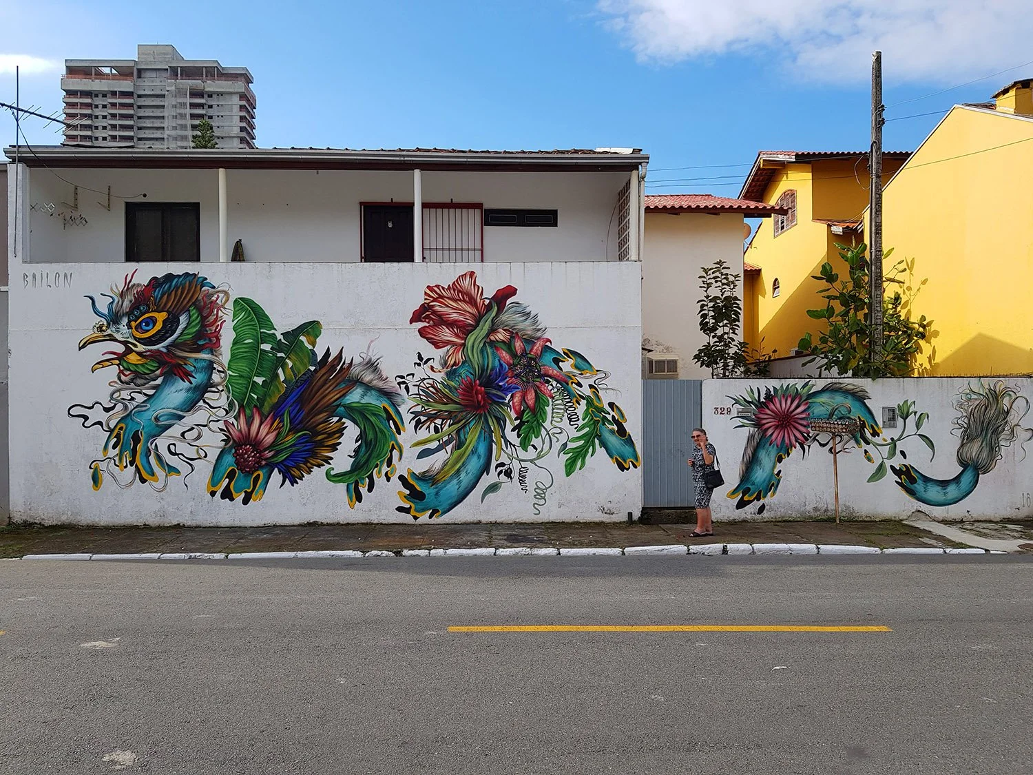 Colorful mural of a dragon intertwined with flowers on a white wall, with a woman standing nearby.