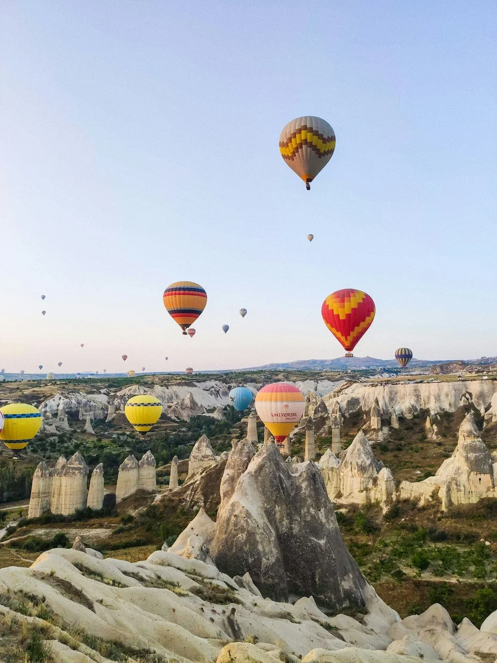 Multiple colorful hot air balloons flying over a rocky landscape with unique formations in the background.