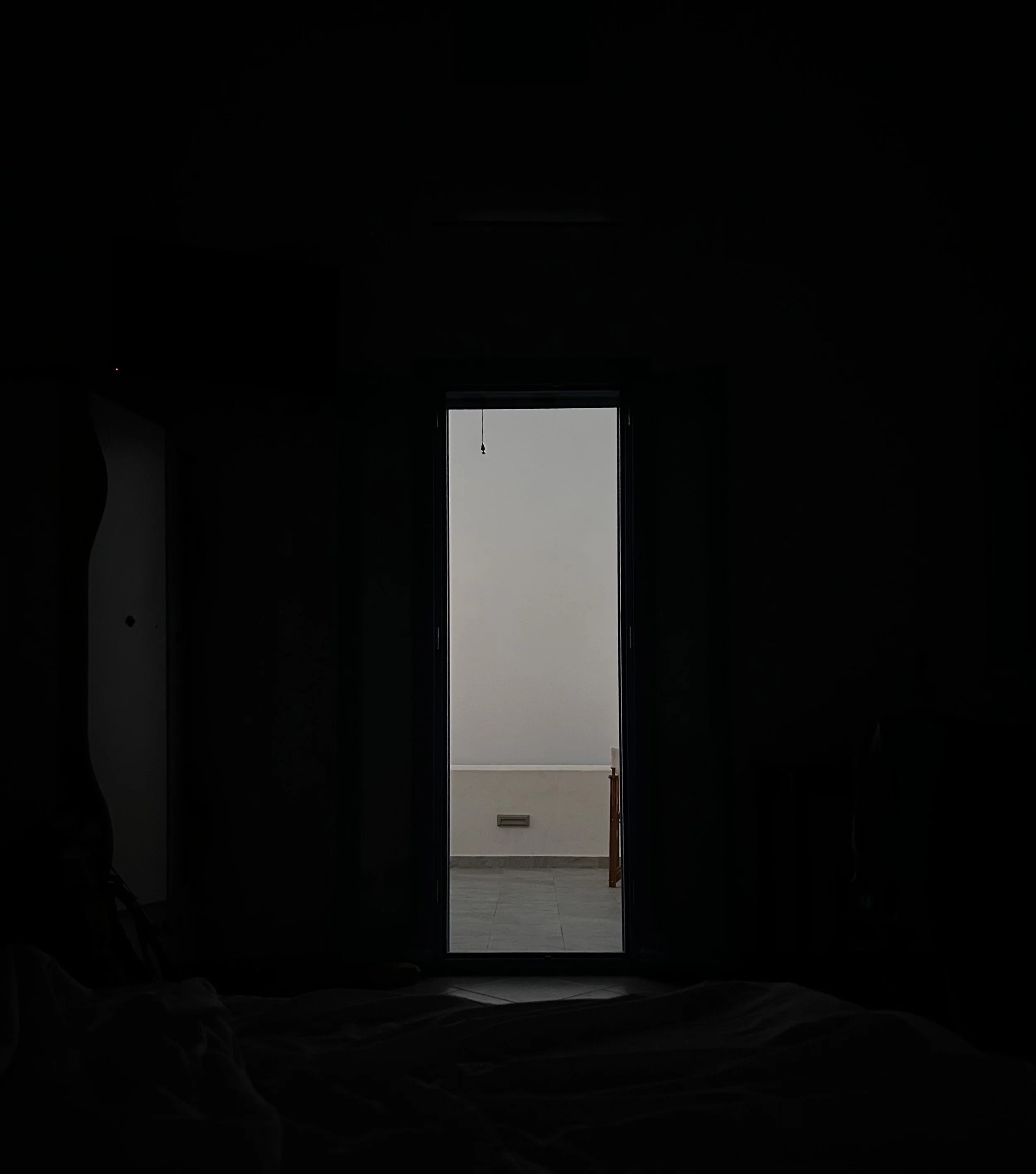 View of a door opening to a room with gray walls and tiled flooring, with natural light coming in through the open door.