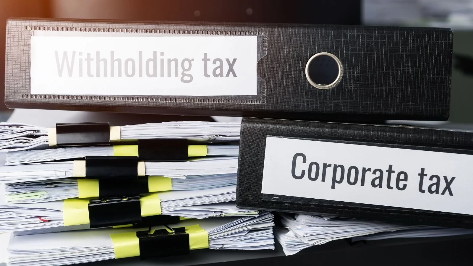 Stacks of papers and binders labeled 'Withholding tax' and 'Corporate tax' on a desk.