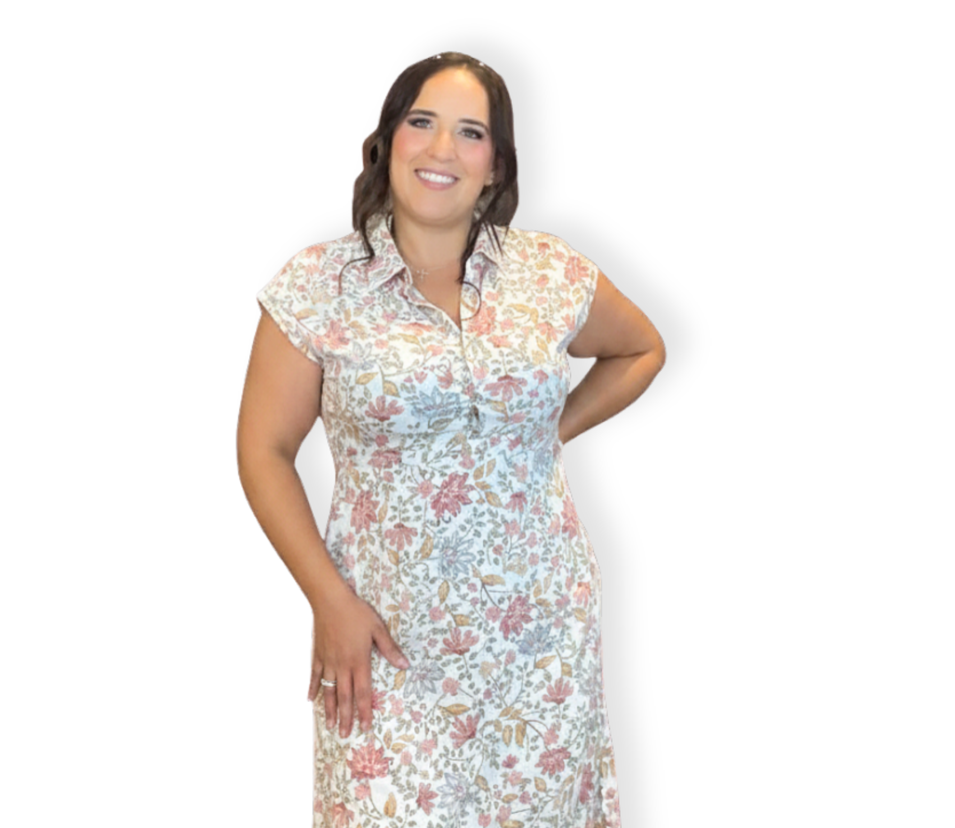 A woman with dark brown hair styled in loose waves, smiling and wearing a short-sleeved, white dress with a pink and beige floral pattern, standing with one hand on her hip against a black background.