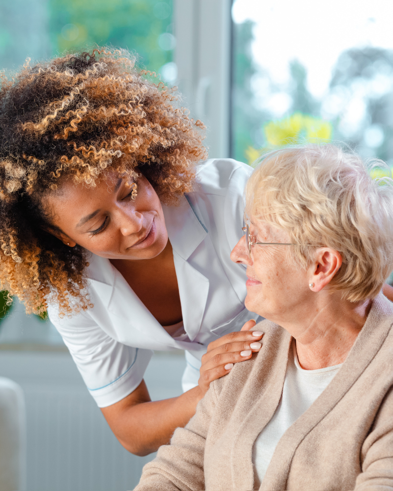 A caregiver talking to an elderly woman in a nursing home or healthcare setting.