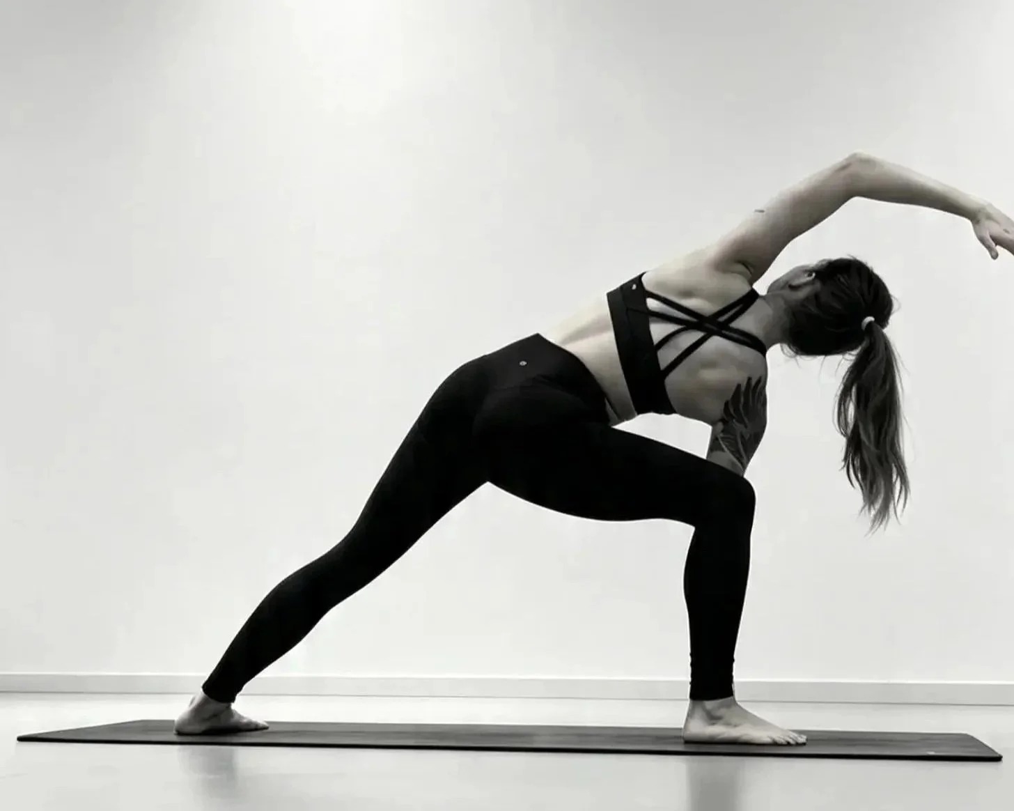 Frau macht Yoga im Halbdreh, auf einer Matte vor weißer Wand, schwarze Sportkleidung, lange Haare, in einer stabilen Position