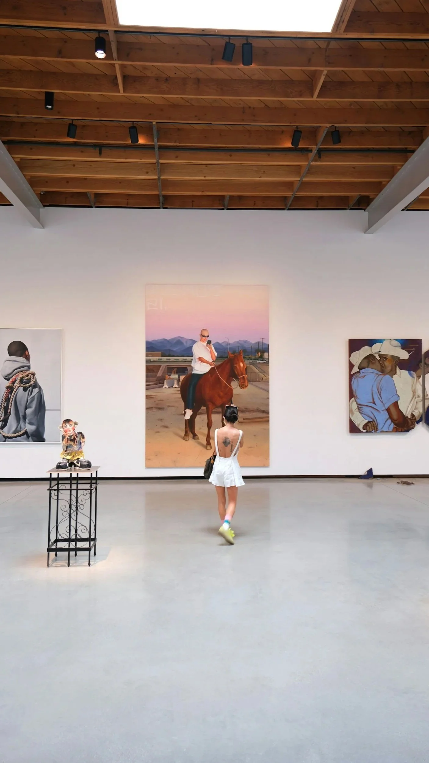 An art gallery with paintings on the wall and a person walking towards a large portrait of a man on a horse, with other people viewing the artwork.