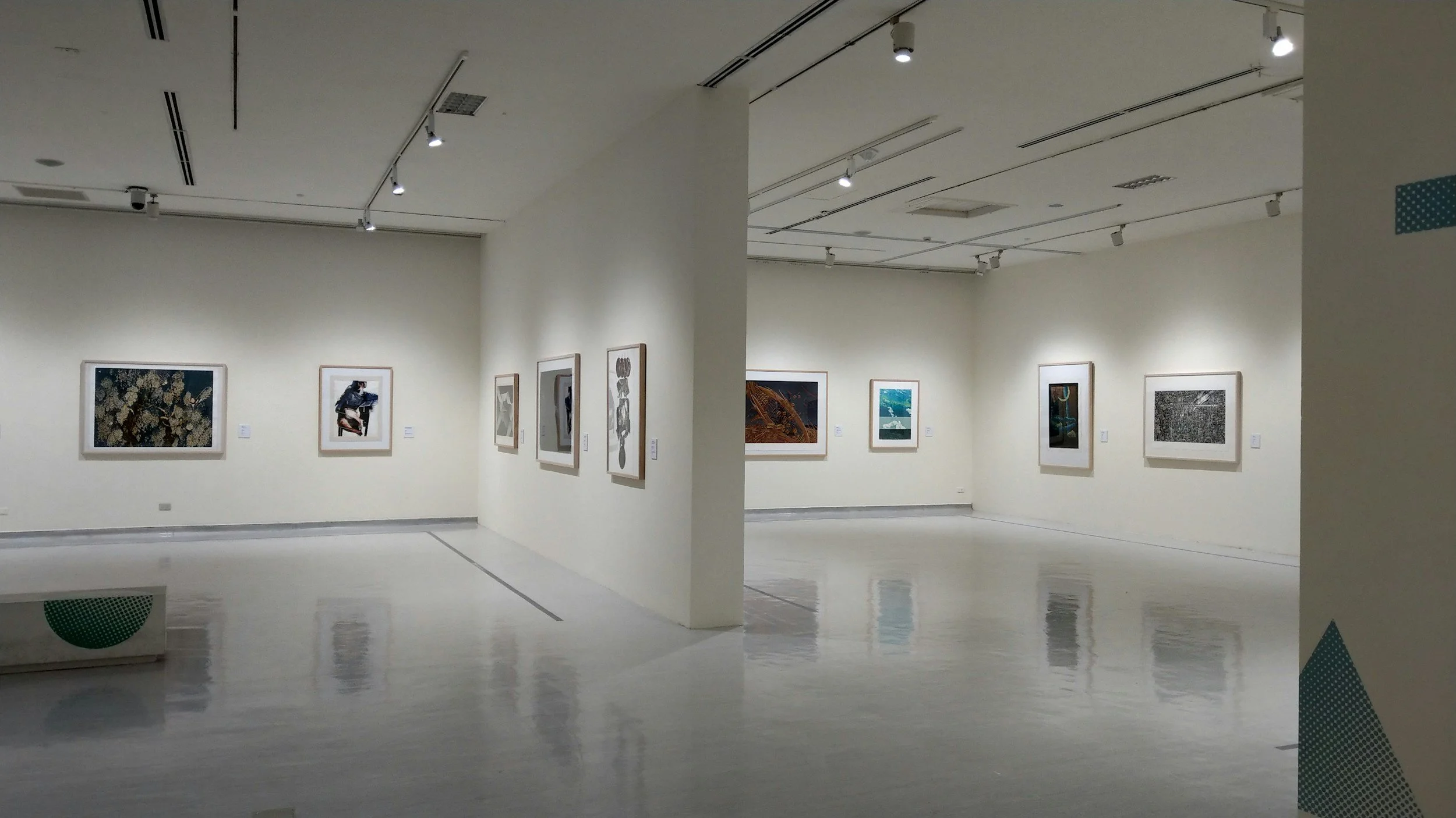 Photo of an art gallery with framed pictures hung on white walls under bright ceiling lights.