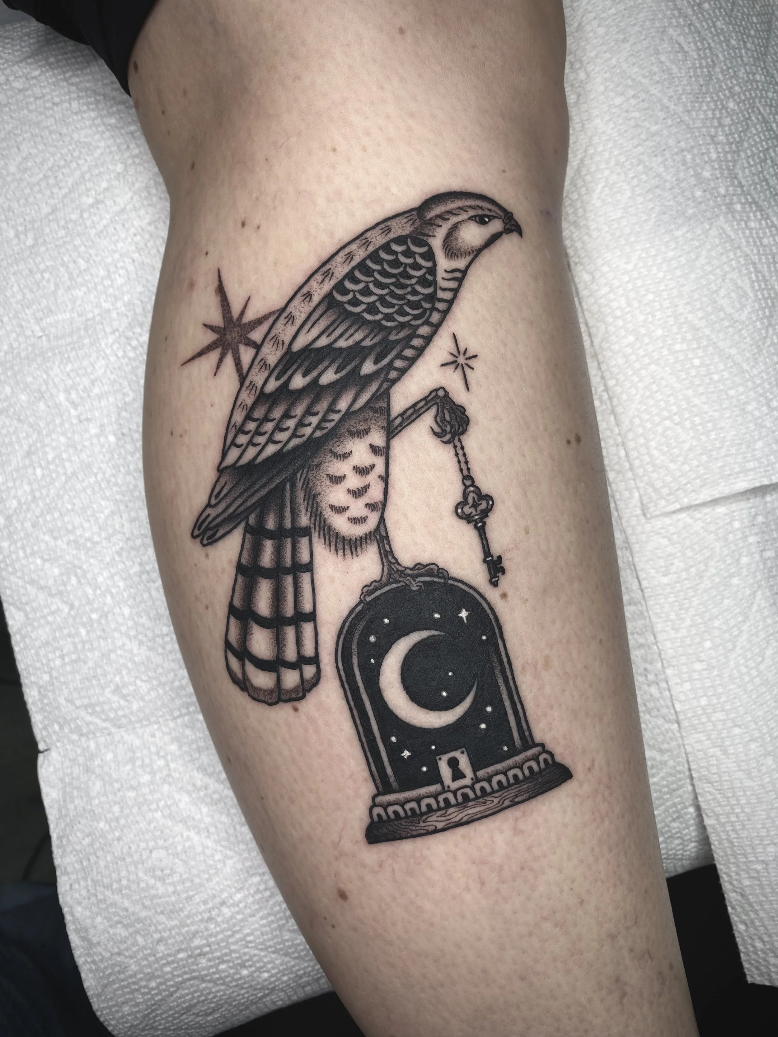 Tattoo of a bird perched on a clock with celestial symbols on a person's arm.