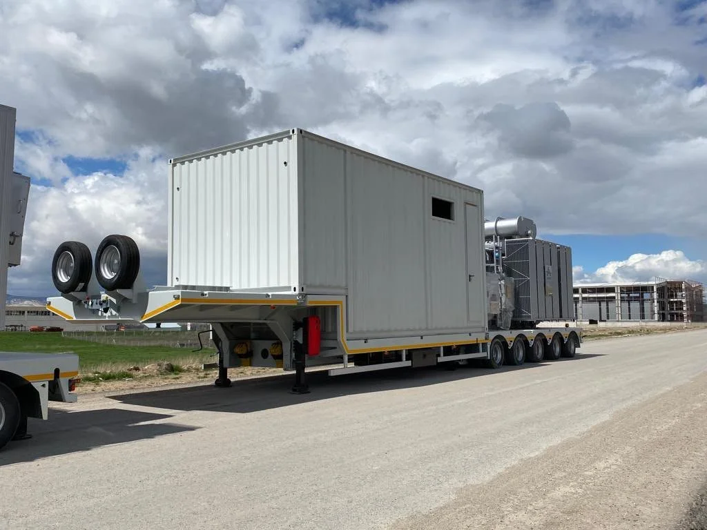 Large white industrial trailer with spare tires and mounted equipment parked on a paved road under a cloudy sky