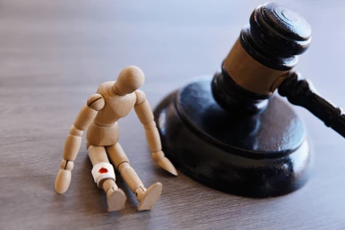 A wooden mannequin doll sitting next to a judge's gavel on a wooden surface.