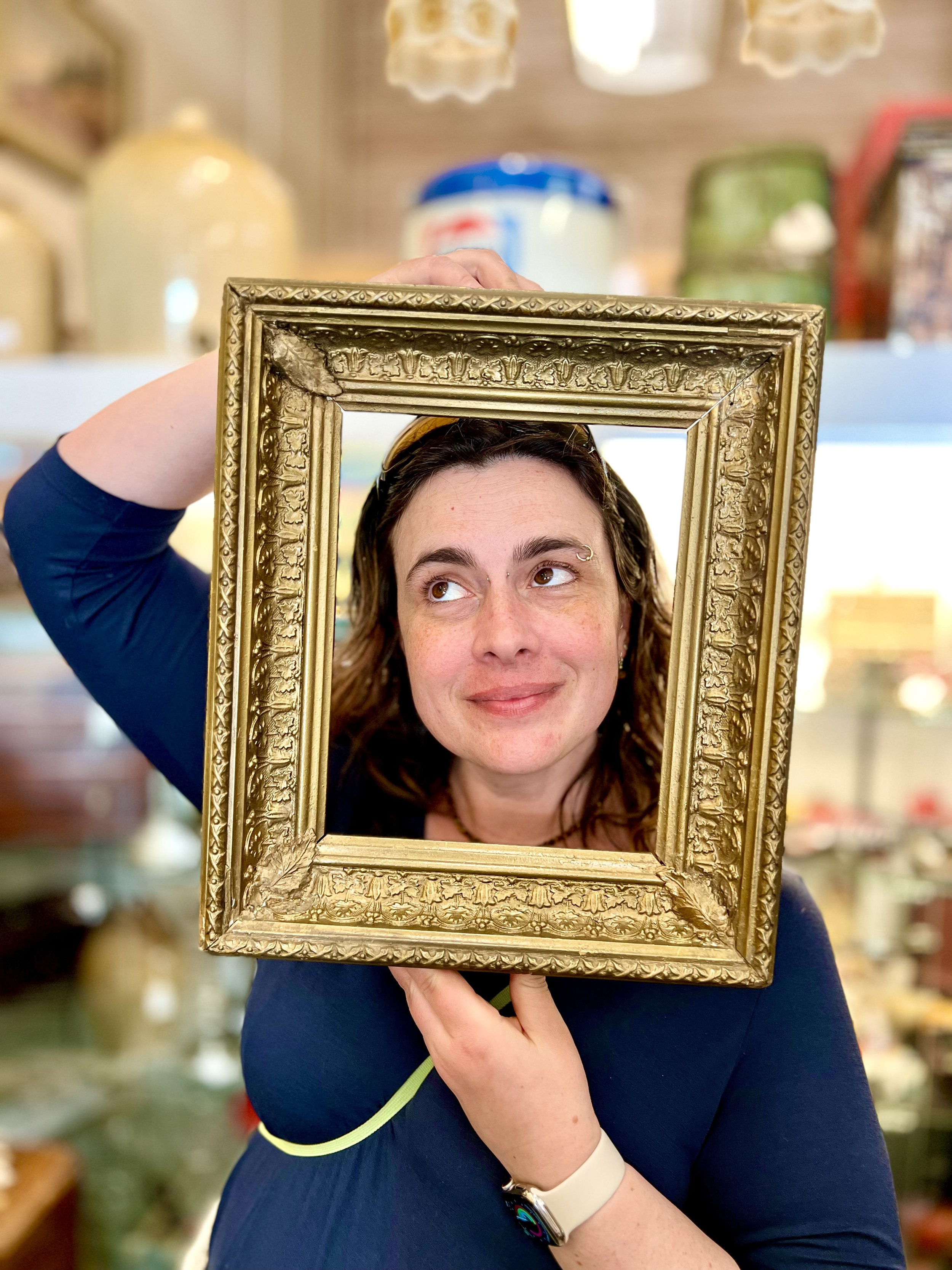 Kate holding a gilded frame up so that it creates the illusion of a portrait of her face, which is playfully looking up.