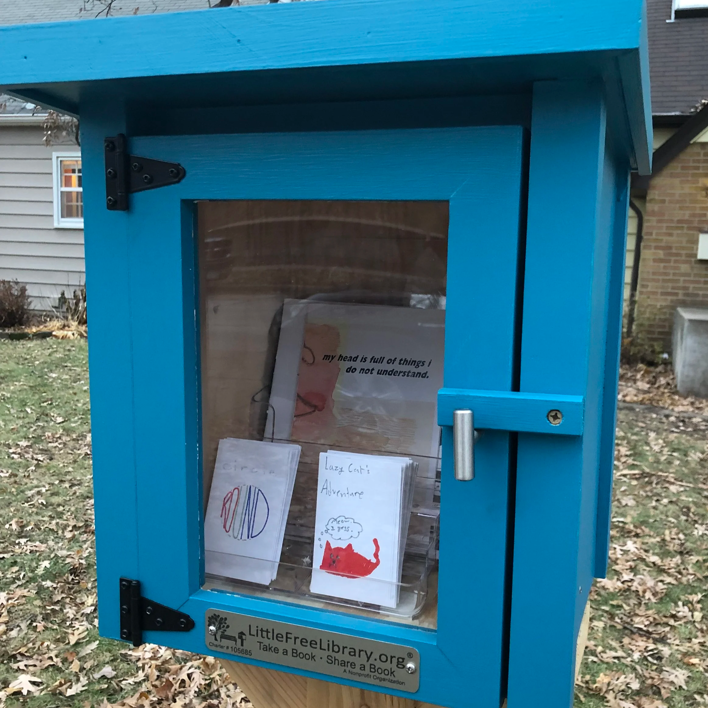 Blue free little library in a front yard filled with zines.