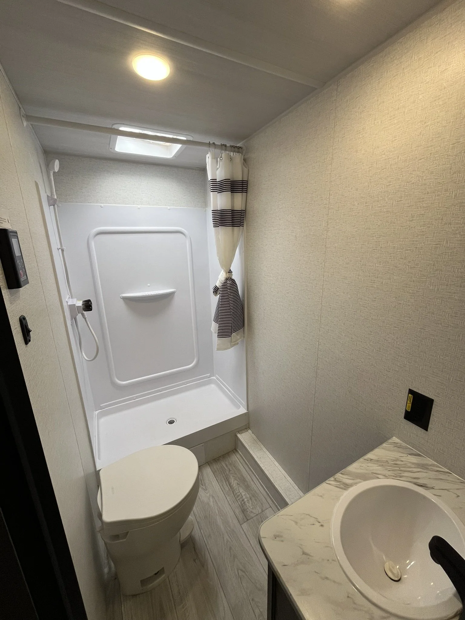 Bathroom with shower stall, toilet, and sink, with beige walls, a skylight, and a curtain in black and white stripes.