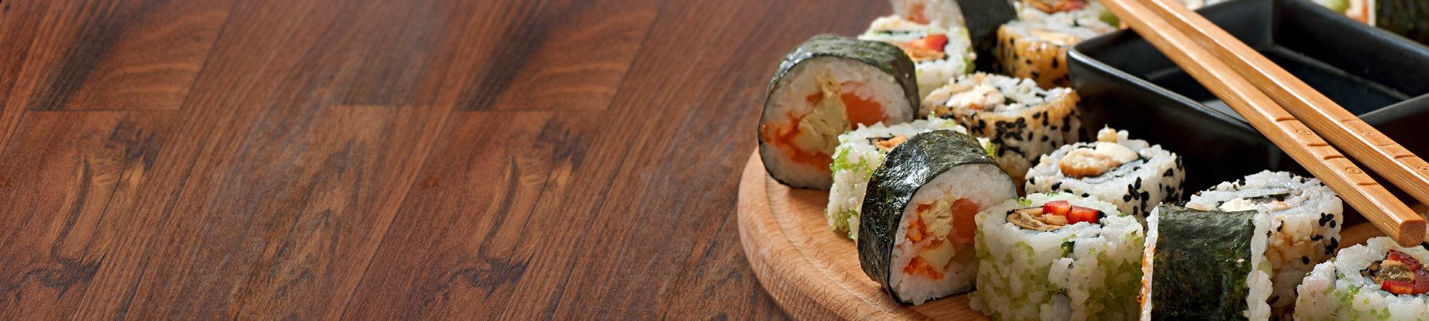 Assorted sushi rolls on a wooden platter with chopsticks, on a wooden table.