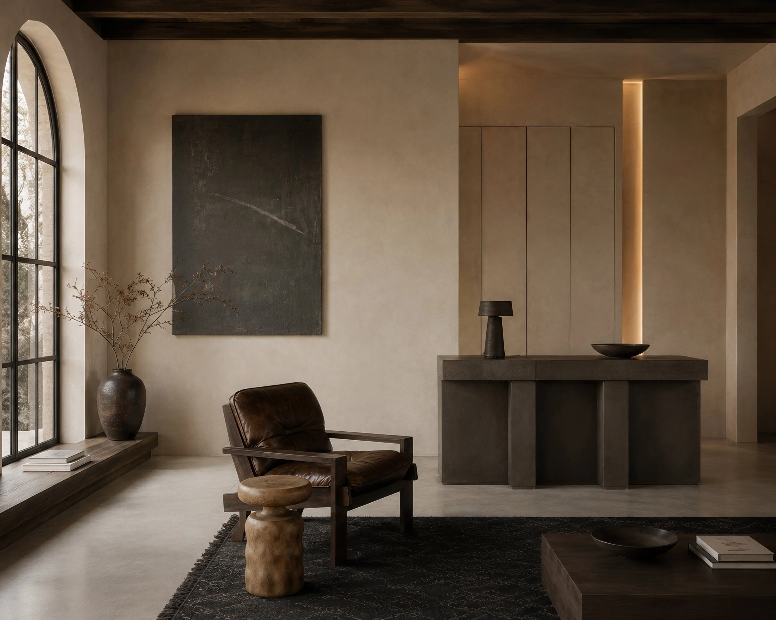 Interior of a modern living room with a large arched window, beige walls, a dark textured art piece, a leather armchair, a wooden stool, and decorative items including a black vase and a bowl.