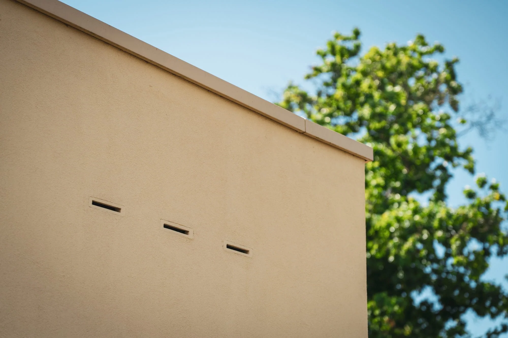 Minimal beige exterior wall with small facade openings and crisp architectural detailing