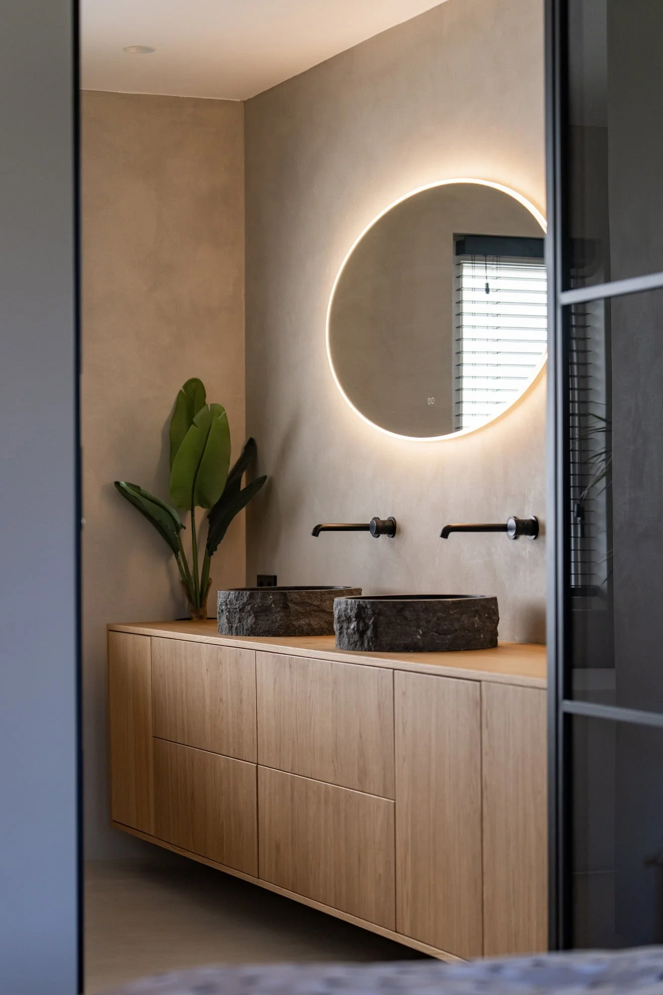 Bathroom vanity with oak cabinetry, round illuminated mirror and black tapware