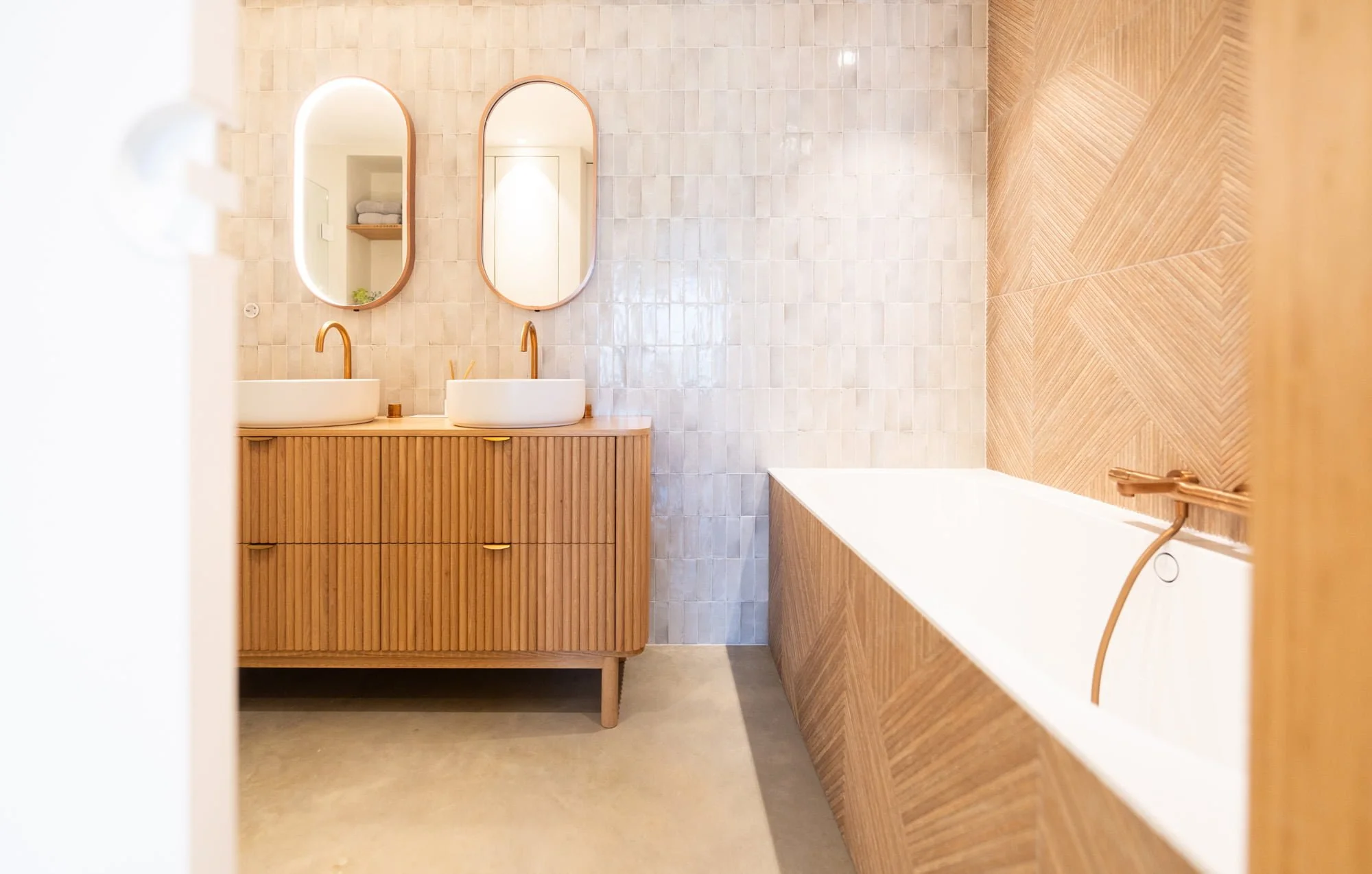 Warm bathroom interior with oak vanity, white bathtub and natural stone tile finish