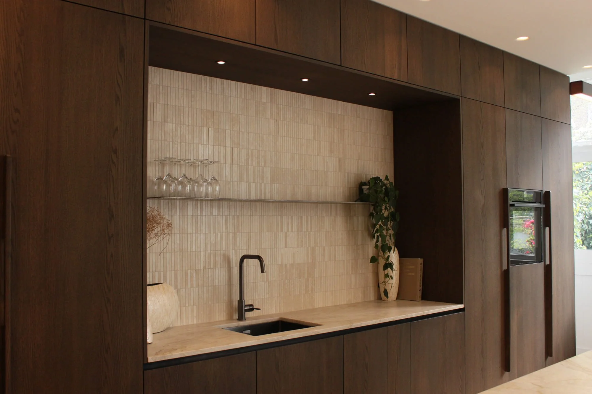 Compact dark wood kitchenette with textured backsplash, stone worktop and warm ambient lighting