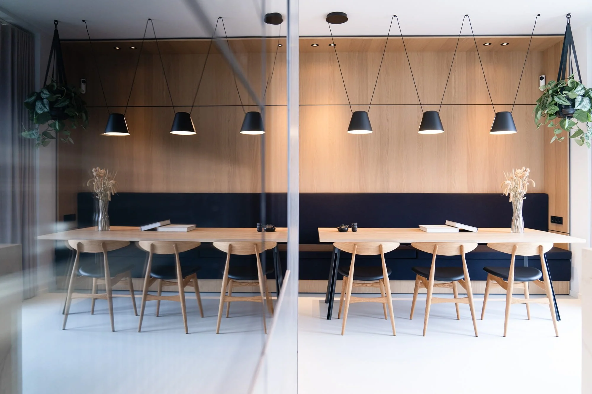 Dining area with long table, light oak wall panelling and black pendant lighting