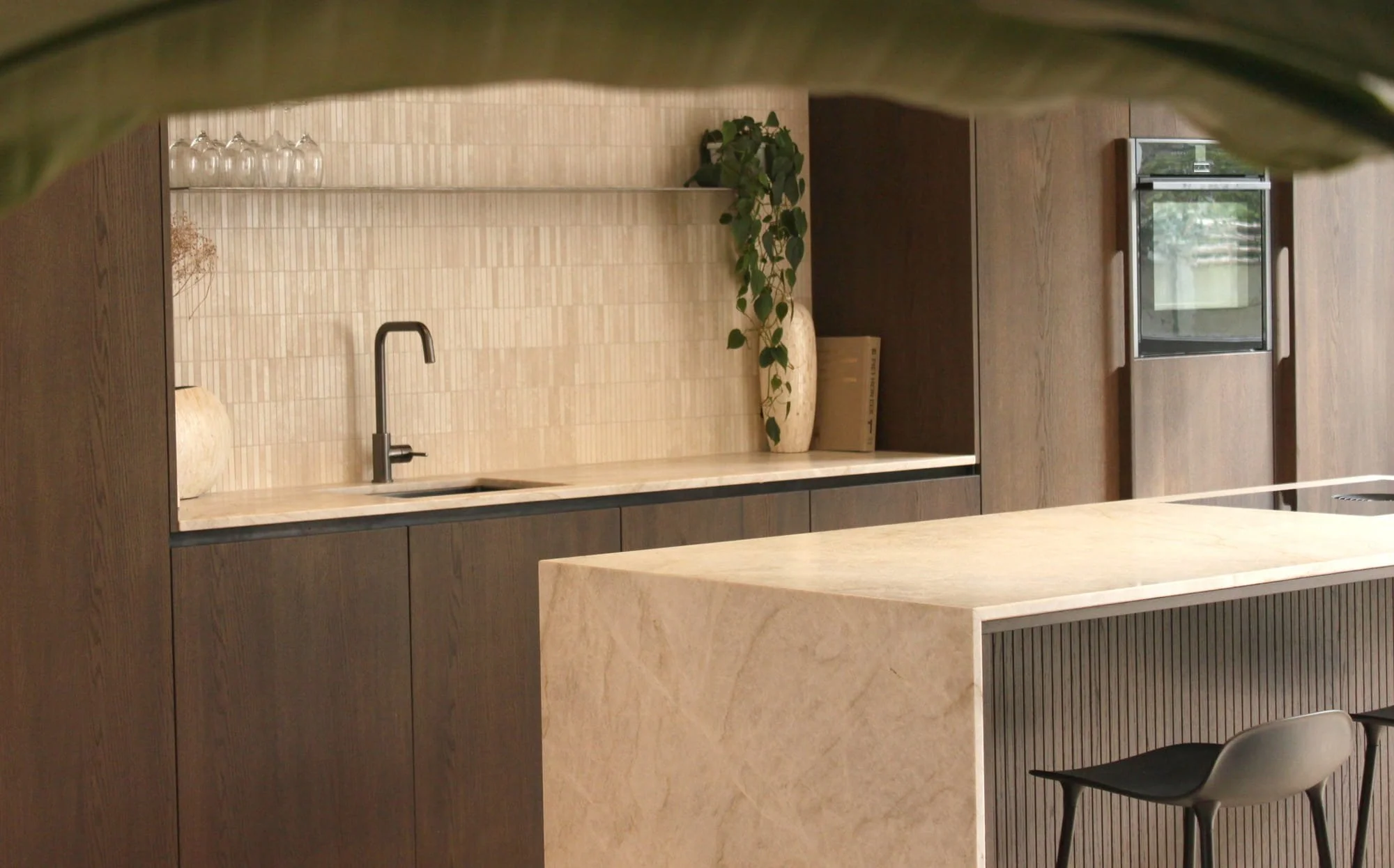 Warm minimalist kitchenette with textured stone worktop, dark wood cabinetry and soft natural styling