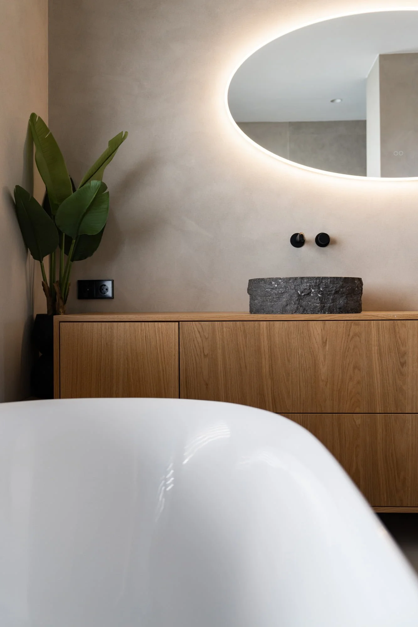Warm bathroom interior with freestanding bathtub, oak vanity and textured grey wall finish