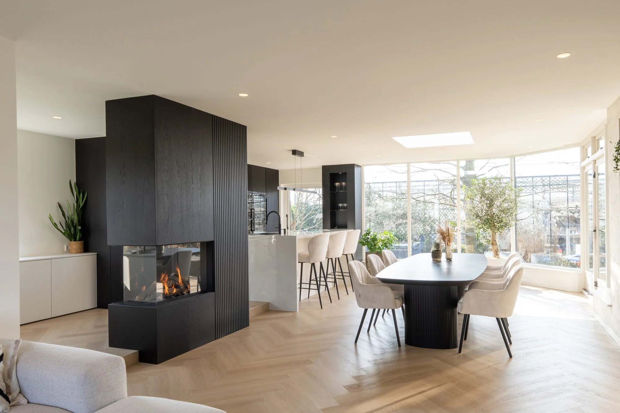 Open living space with dark kitchen cabinetry, oak flooring and soft garden views