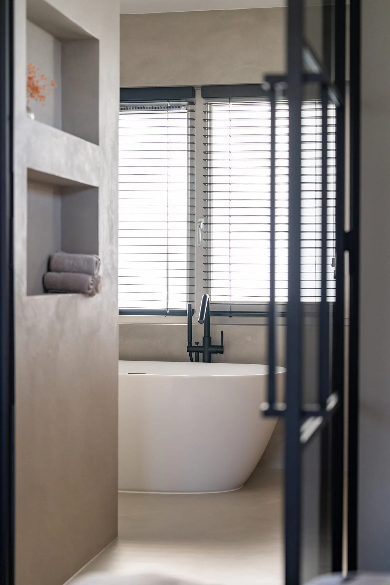 Bathroom view with freestanding bathtub, black framed glass door and shuttered window