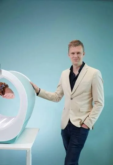 A person holding a wooden sample in front of a display of different wood samples and ceramic tiles on a white wall with a brick pattern.