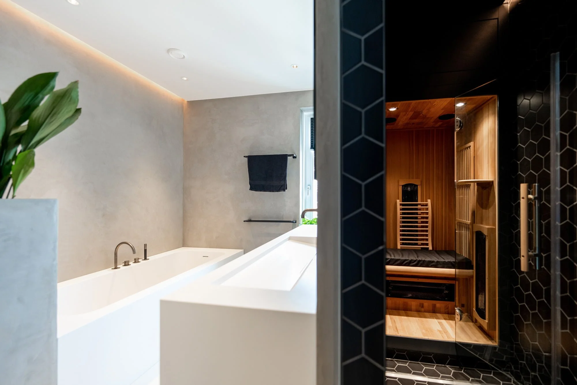 Minimal bathroom with white bathtub, textured wall finish and dark stone shower area