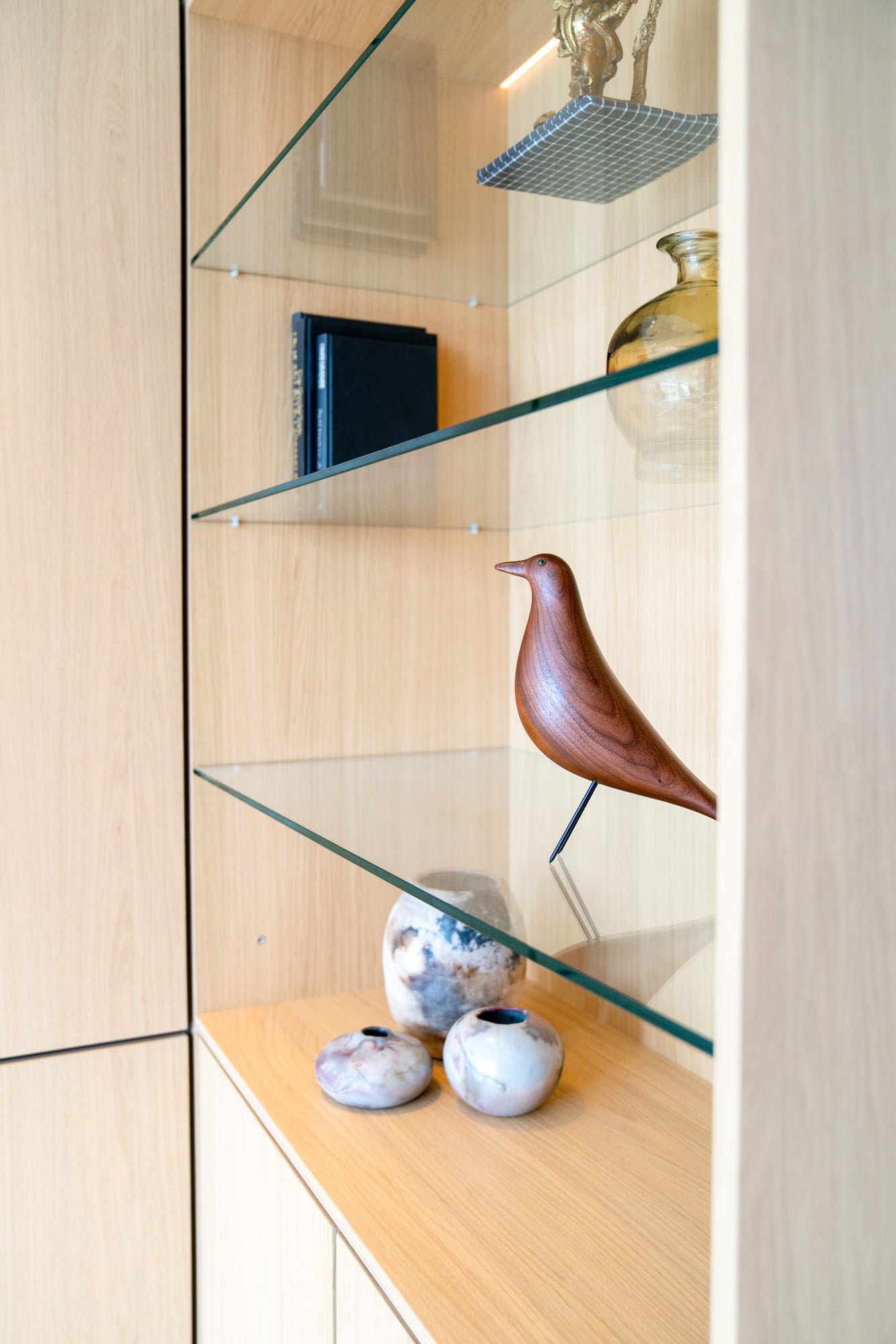 Close up of oak shelving with curated objects, glass shelf and warm material details