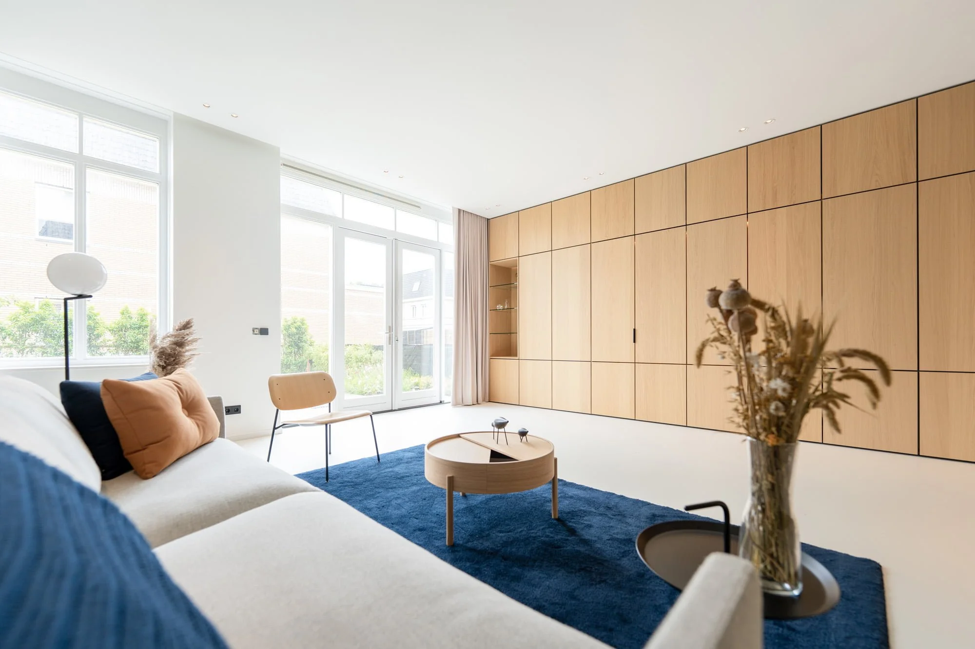 Bright living room with bespoke oak wall cabinetry, soft blue sofa and natural daylight