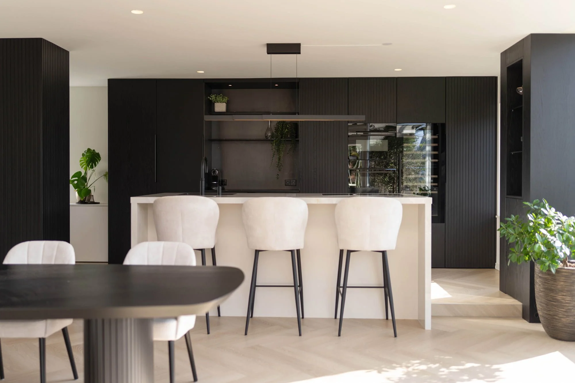 Modern kitchen with white island, dark cabinetry, bar stools and natural daylight