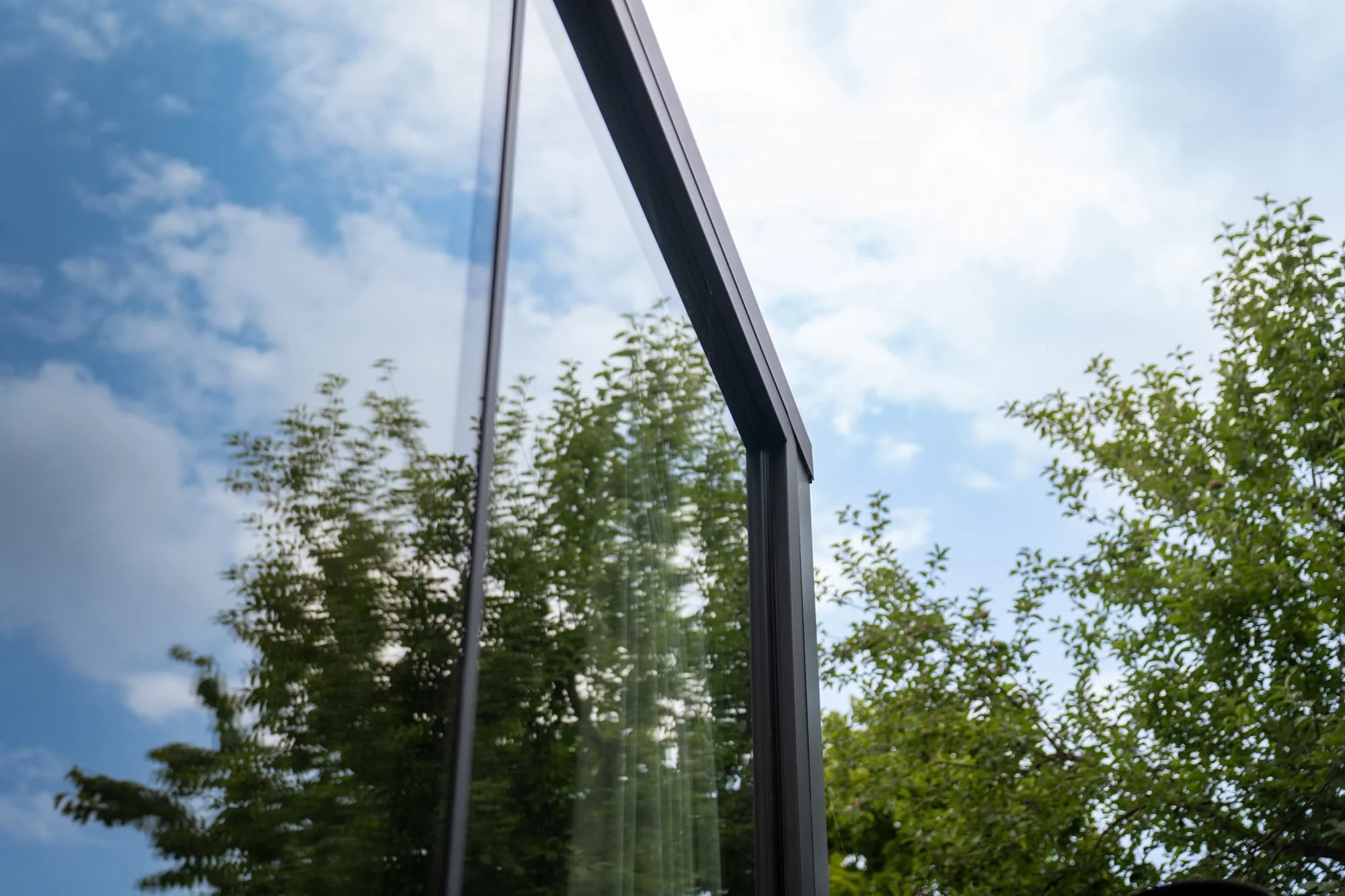 Glass facade detail with slim black framing, garden reflections and lush greenery
