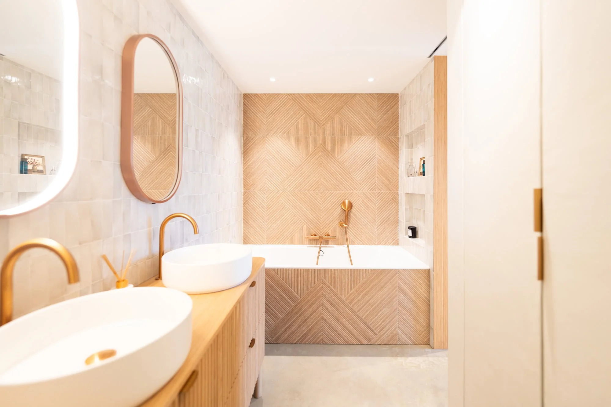 Bathroom with freestanding bathtub, round mirror, oak vanity and textured wall tiles