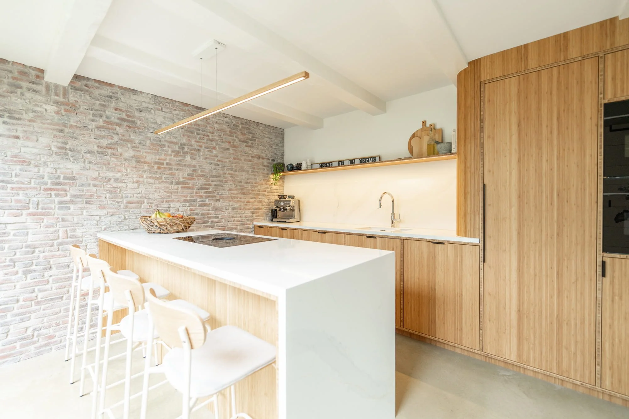 Bright open kitchen with white island, oak cabinetry and exposed brick wall
