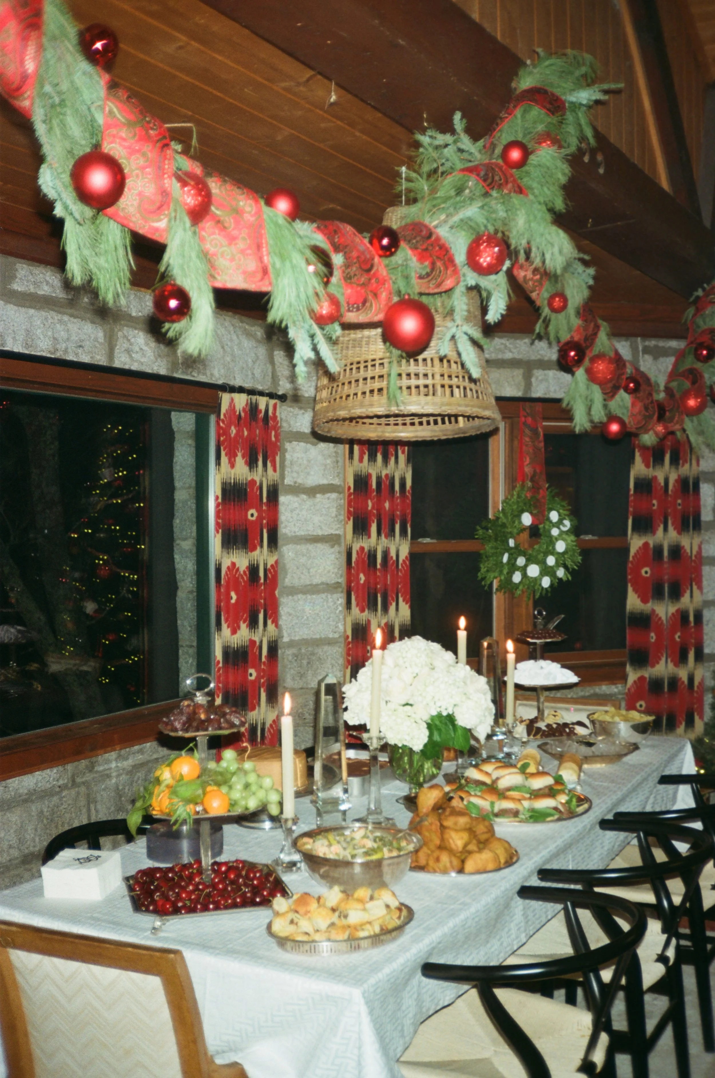 Christmas decorated dining room with a table set for a celebration, featuring food, candles, and festive decorations including garland with red ornaments.