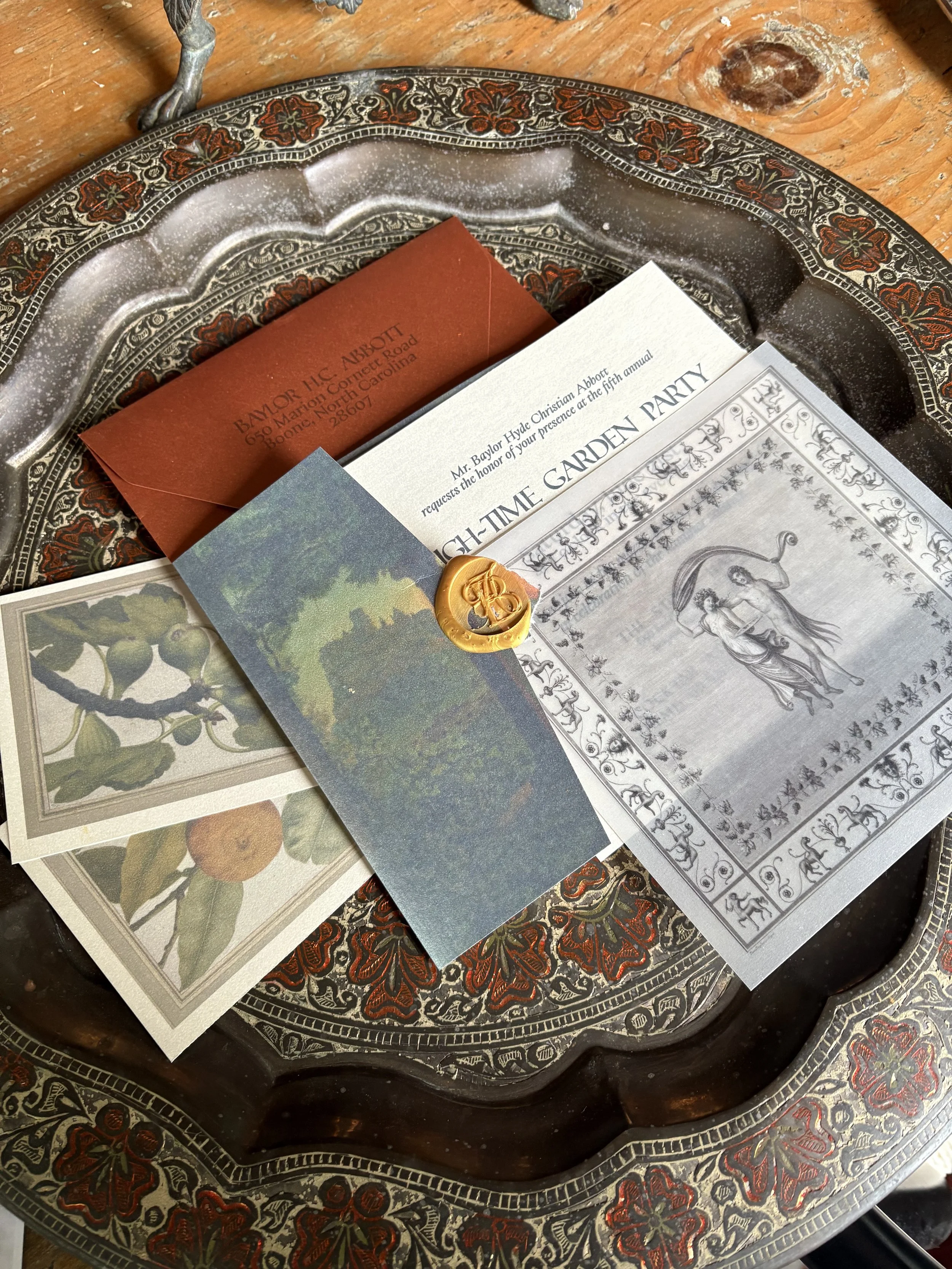 A decorative silver tray holding a red envelope, a white card, and a small card with an image of green apples. The tray has ornate floral engravings and a black background with red accents.